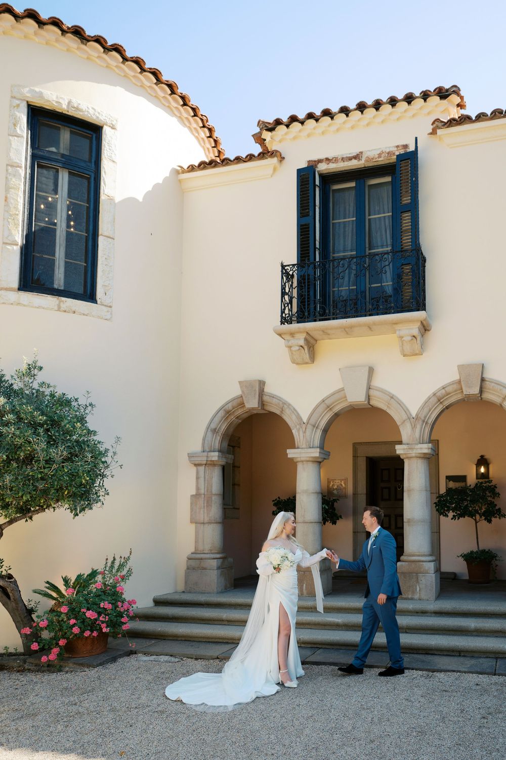 Wedding couple poses in a Mediterranean-style courtyard with arched doorways and cream stucco walls.