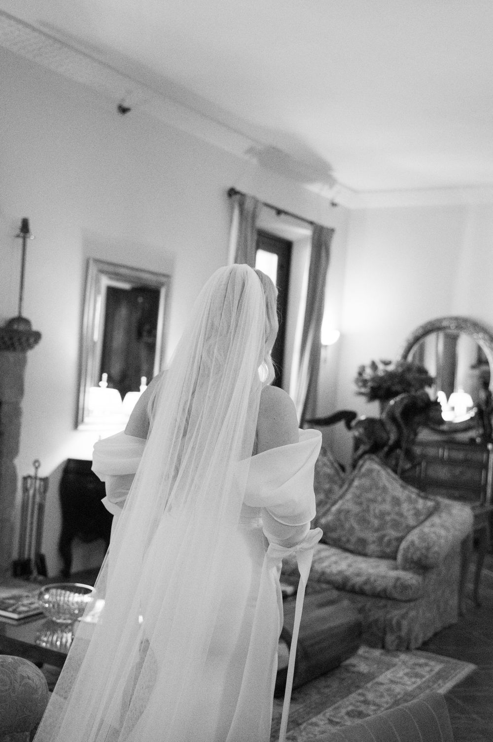 A ghostly figure in white fabric appears in a dimly lit room with vintage furniture and mirrors.