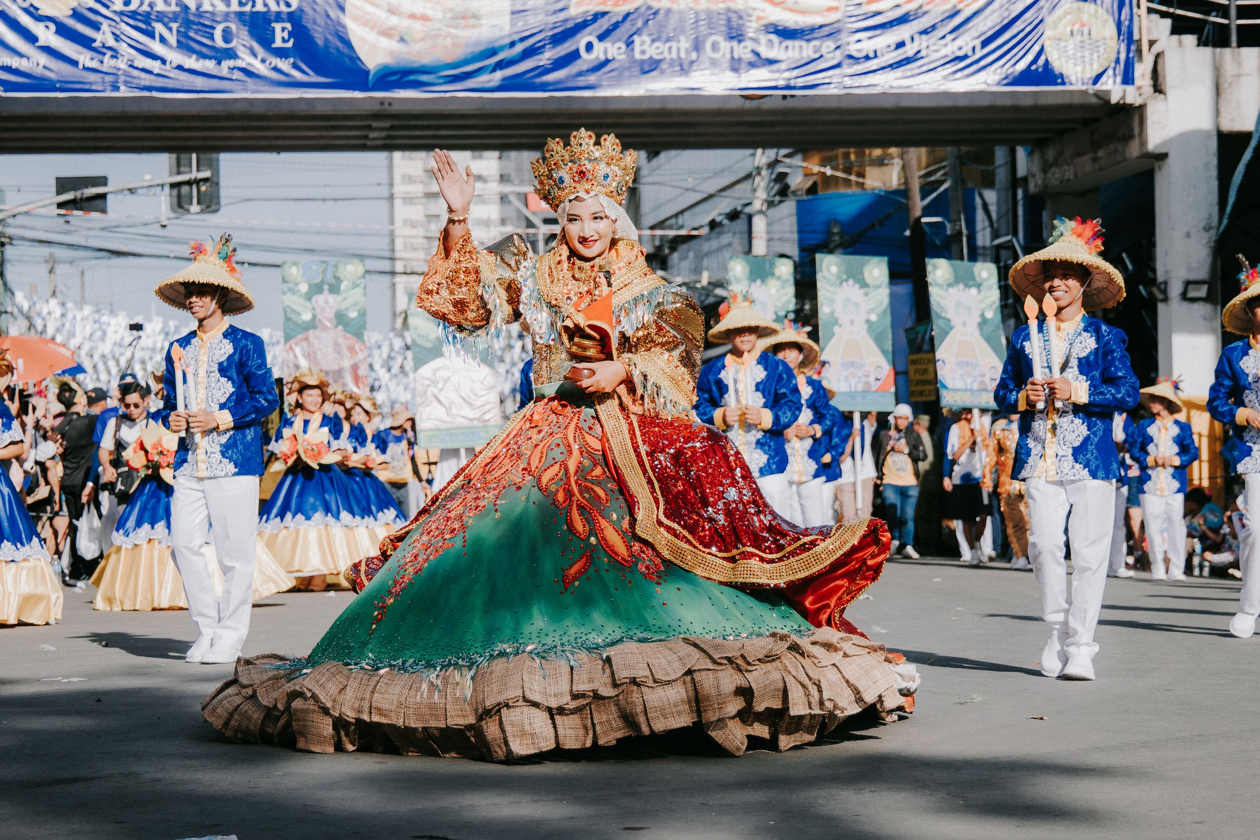 Wide shot of street festival performers in elaborate costumes with spectators lining the route.