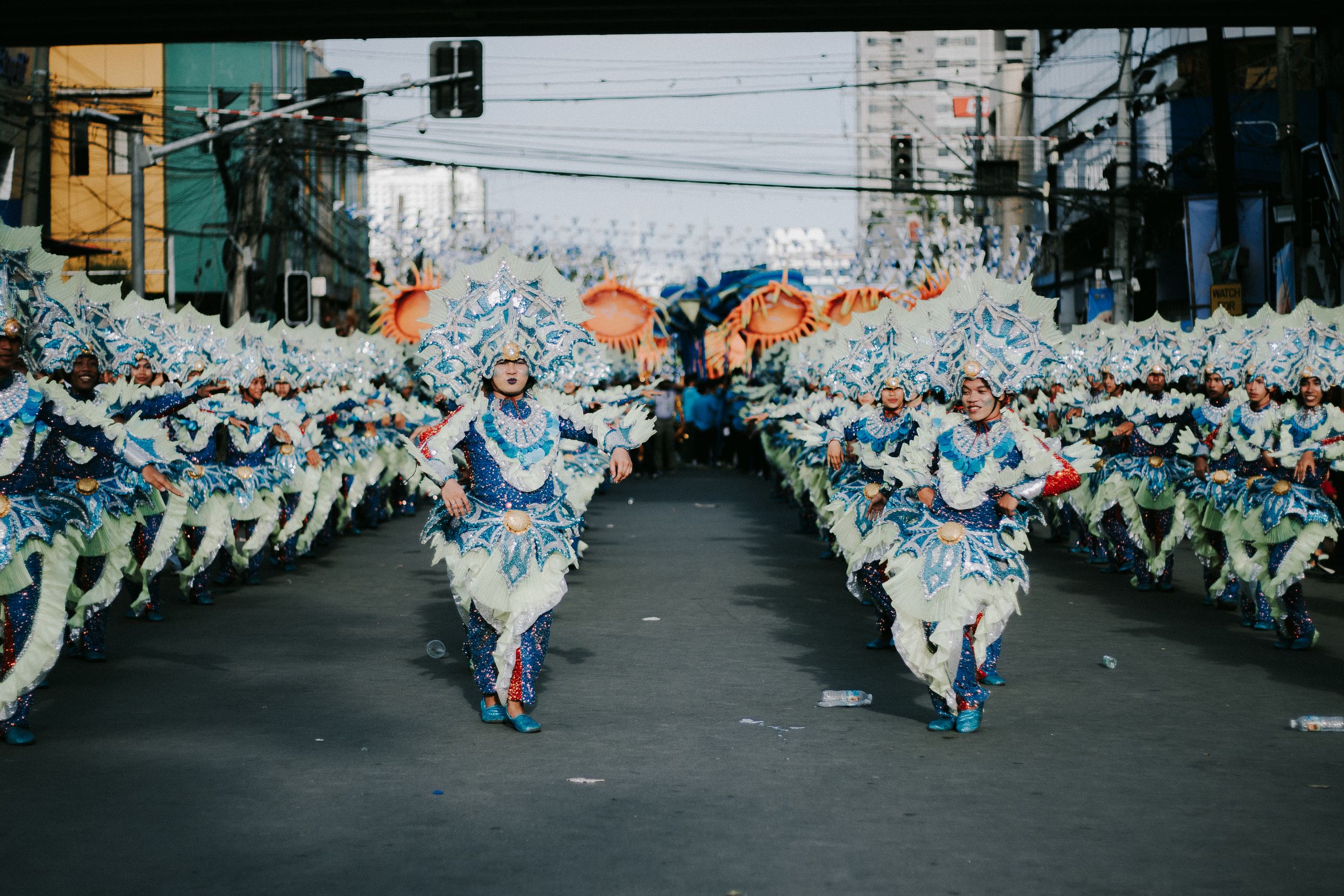 Street performers in light blue costumes dancing in synchronized formation during a festival parade.