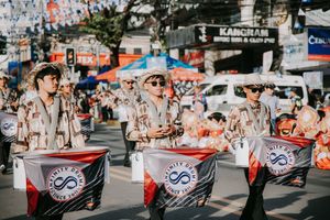 Street parade with performers carrying banners and flags during a festival celebration.
