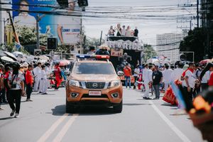 Street view of festival parade route with orange vehicle and crowd barriers.