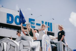 People in white outfits performing coordinated movements against a bright blue sky.