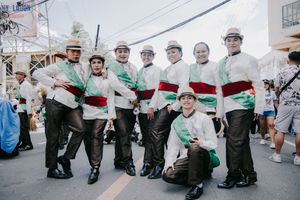 Group of performers in white and red outfits kneeling on the street during a festival parade.