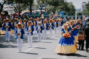 Parade performers in blue and white uniforms marching down a sunny street during a cultural celebration.
