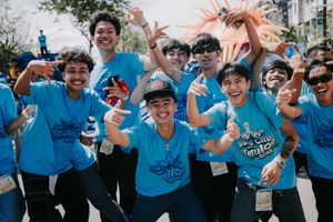 Enthusiastic performers in bright blue t-shirts celebrating during an outdoor street festival.