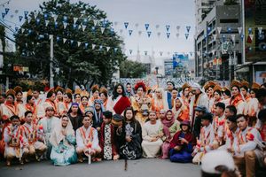 Wide shot of festival performers in colorful costumes lined up along a city street.