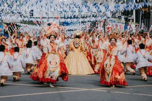 Large group of performers in red and white costumes spread across a city street during a festival.