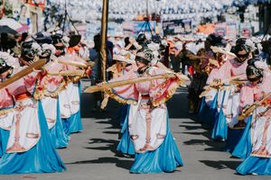 Traditional dancers in pink and blue costumes perform synchronized movements during a street festival.