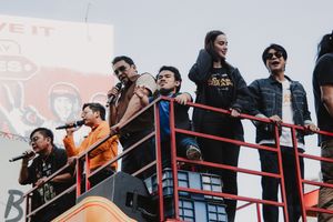 Performers with microphones stand on elevated platform during outdoor event.
