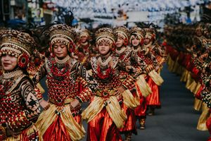 Performers in matching red and gold traditional costumes dance in formation during street parade.