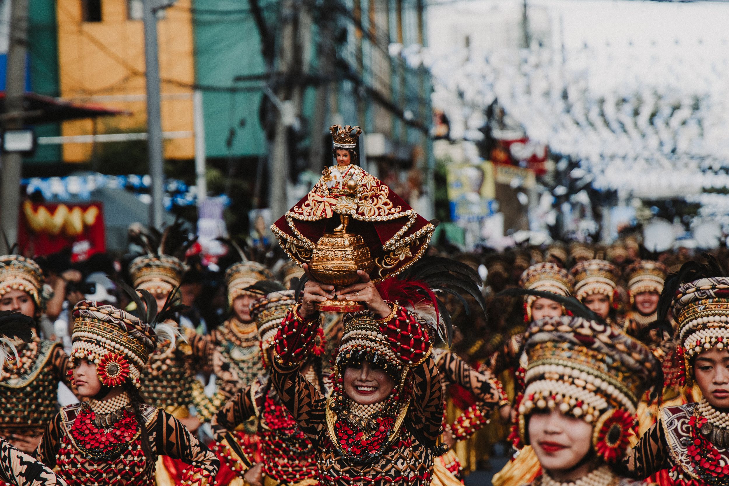 Colorful festival parade featuring performers wearing ornate traditional Filipino costumes and headdresses.