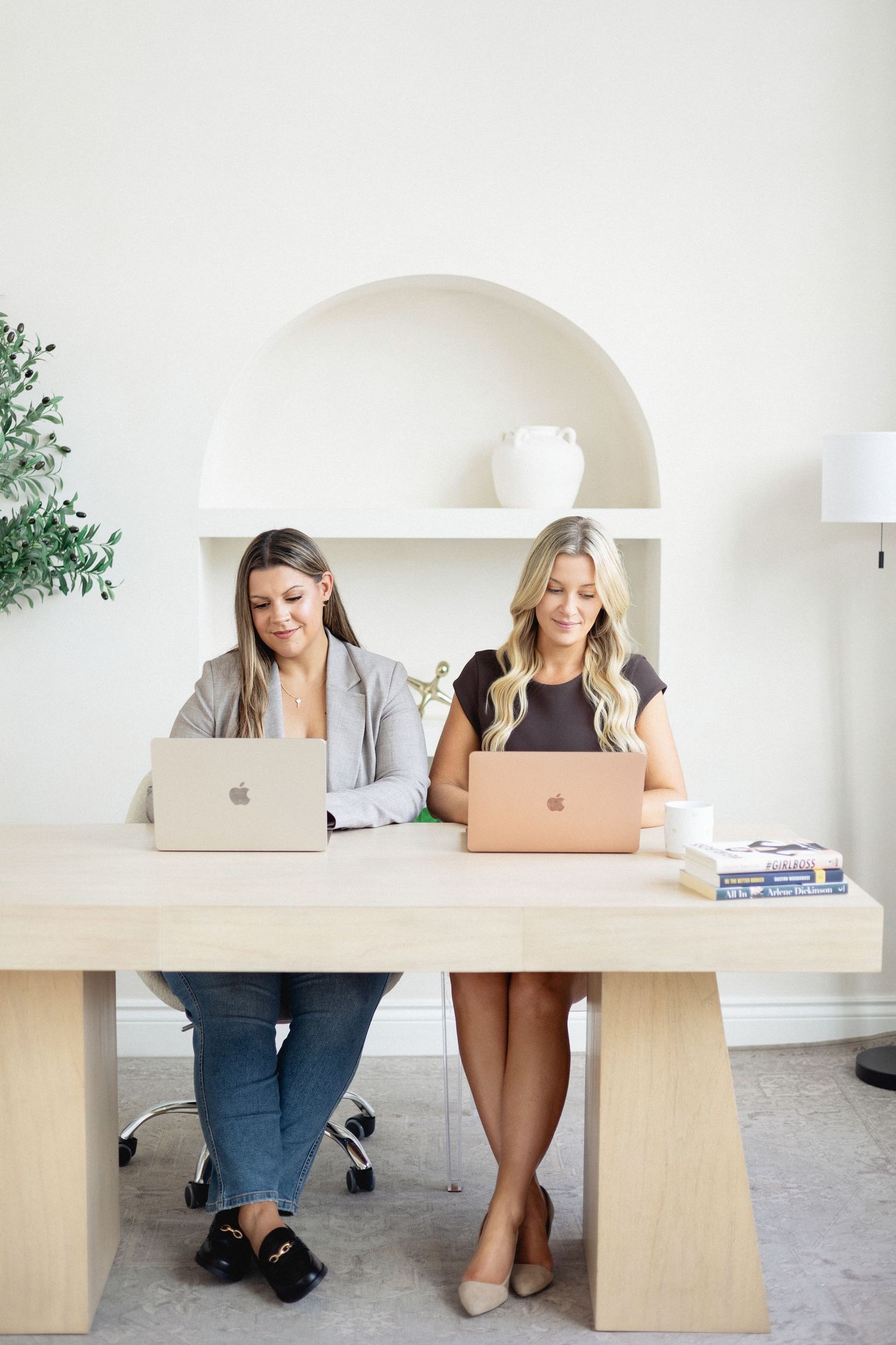Two mortgage brokers during branding photoshoot working as a team on laptops at desk in business attire