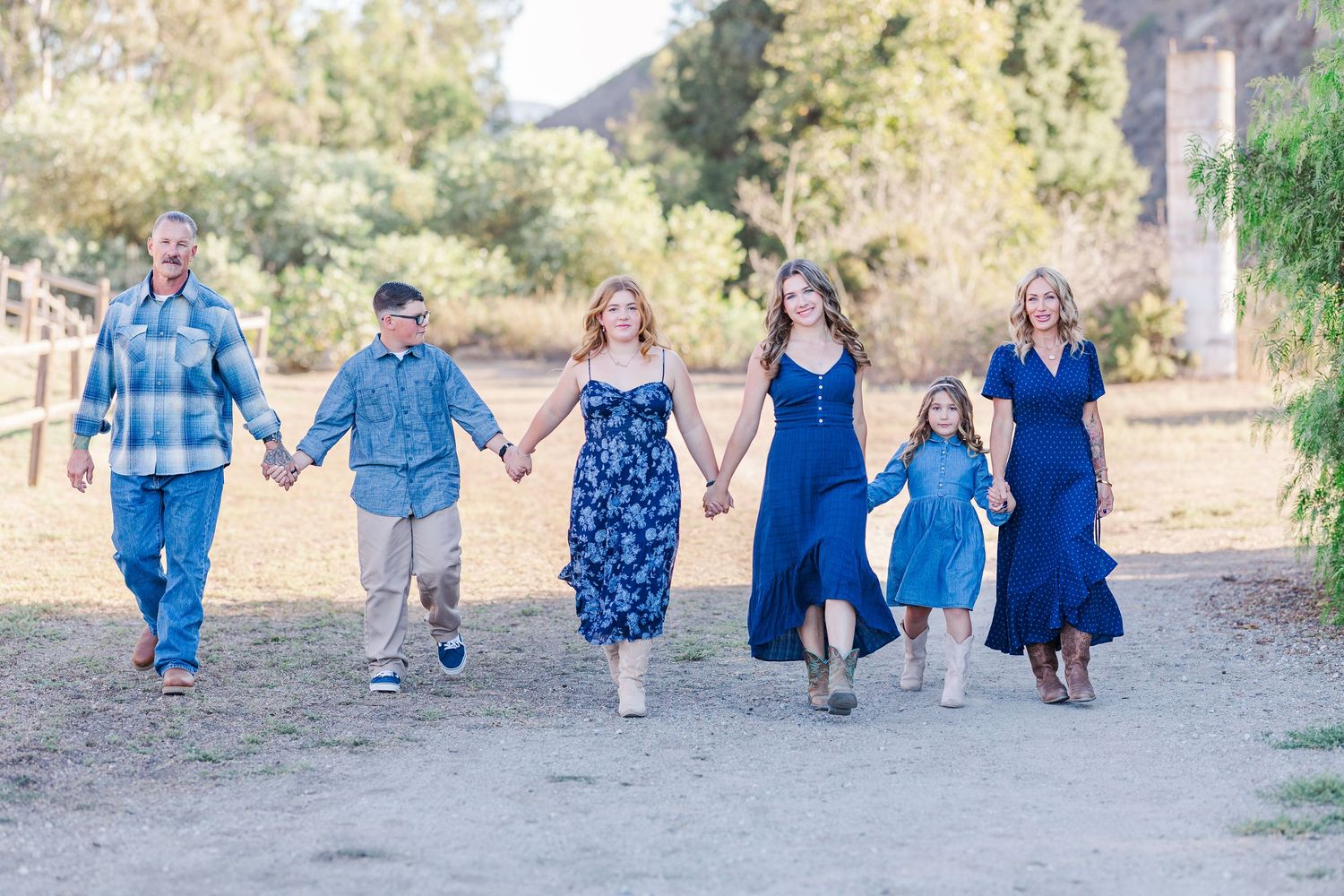 Family members holding hands while walking together on a dirt path in coordinated blue outfits.