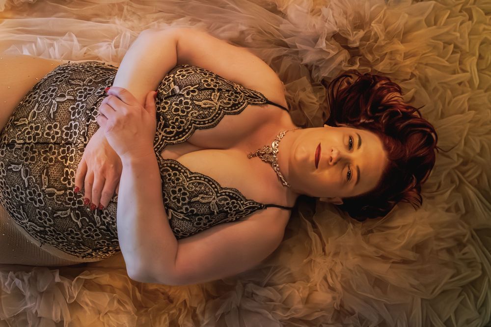 A red-haired woman in leopard print lingerie poses gracefully on a soft, flowing beige fabric backdrop.