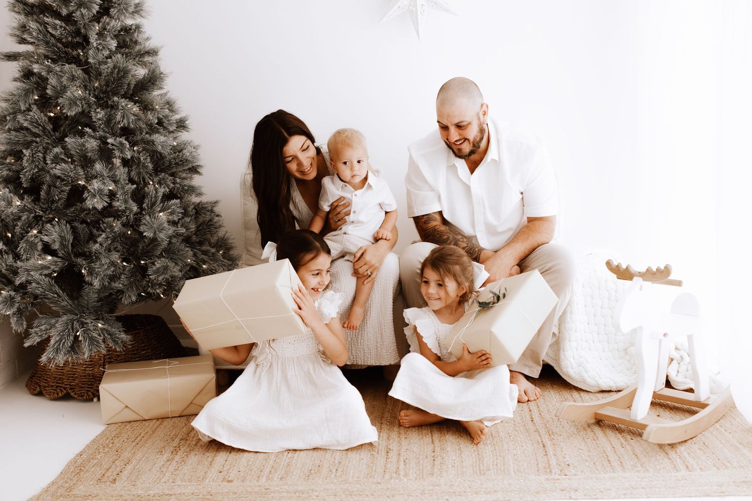 Family in white clothing poses together on floor near holiday decorations.