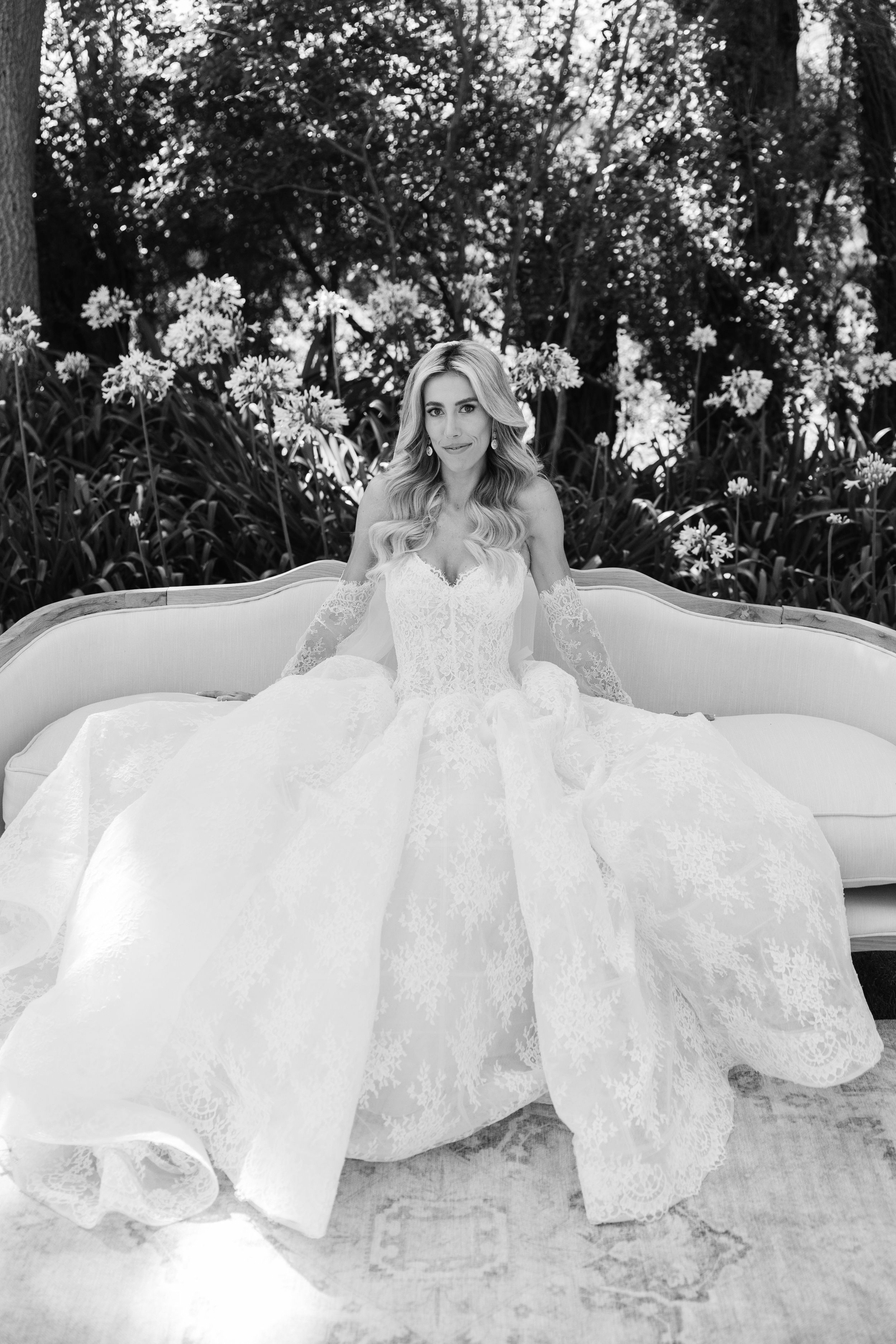 A series of black and white photos showing someone in an elegant flowing white wedding dress posing on a vintage sofa outdoors.