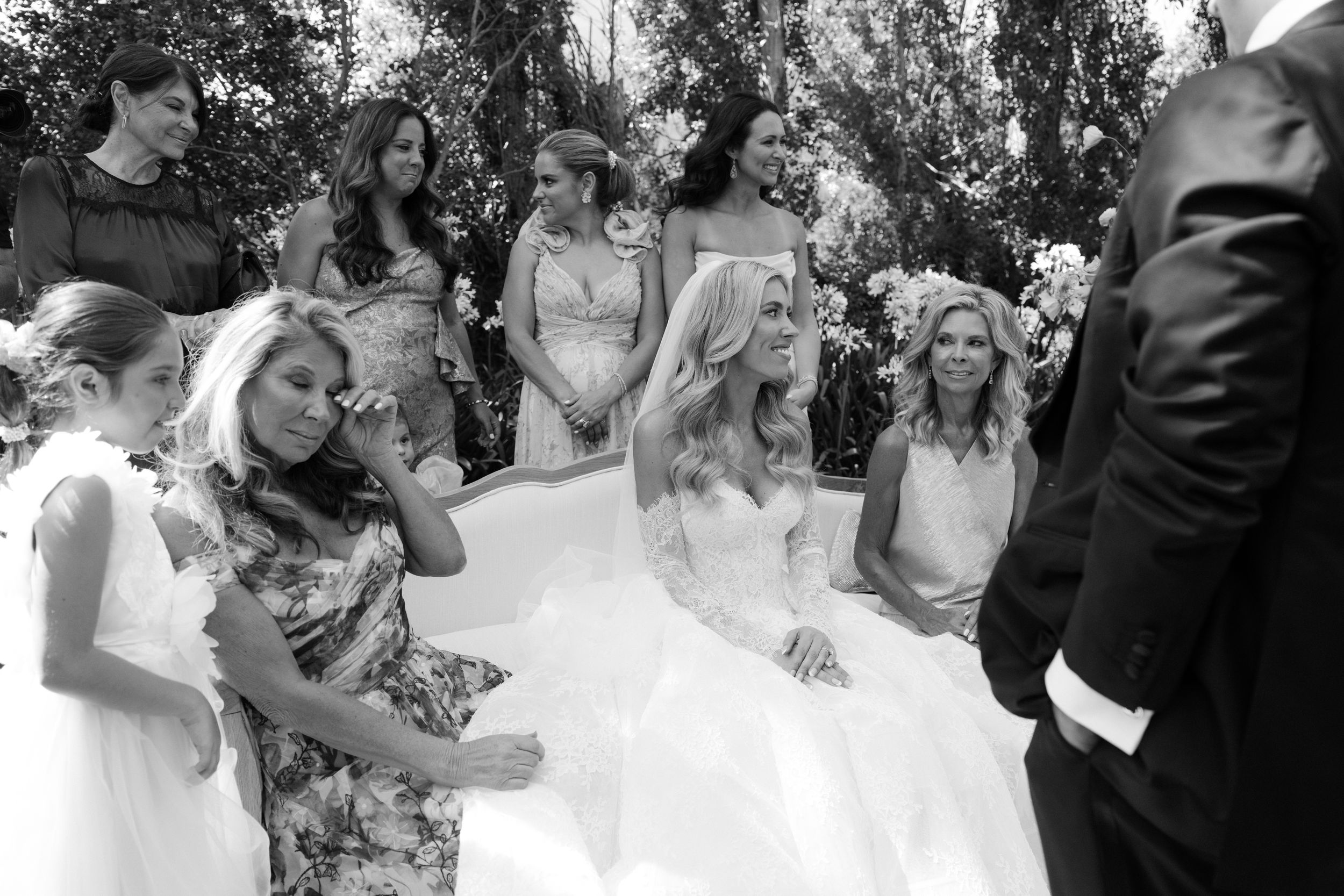 A group of wedding guests laugh and smile together while sitting at an outdoor reception table during a celebration.