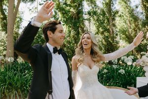 Joyful newlyweds celebrate with raised arms in a sunny garden setting surrounded by lush greenery.