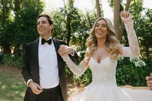 A happy couple in formal wedding attire laughs and celebrates outdoors in a garden setting.