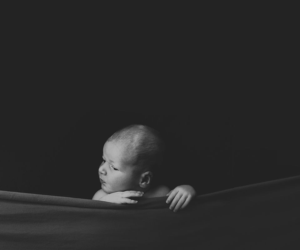 Minimalist newborn photography against dark background with dramatic side lighting.