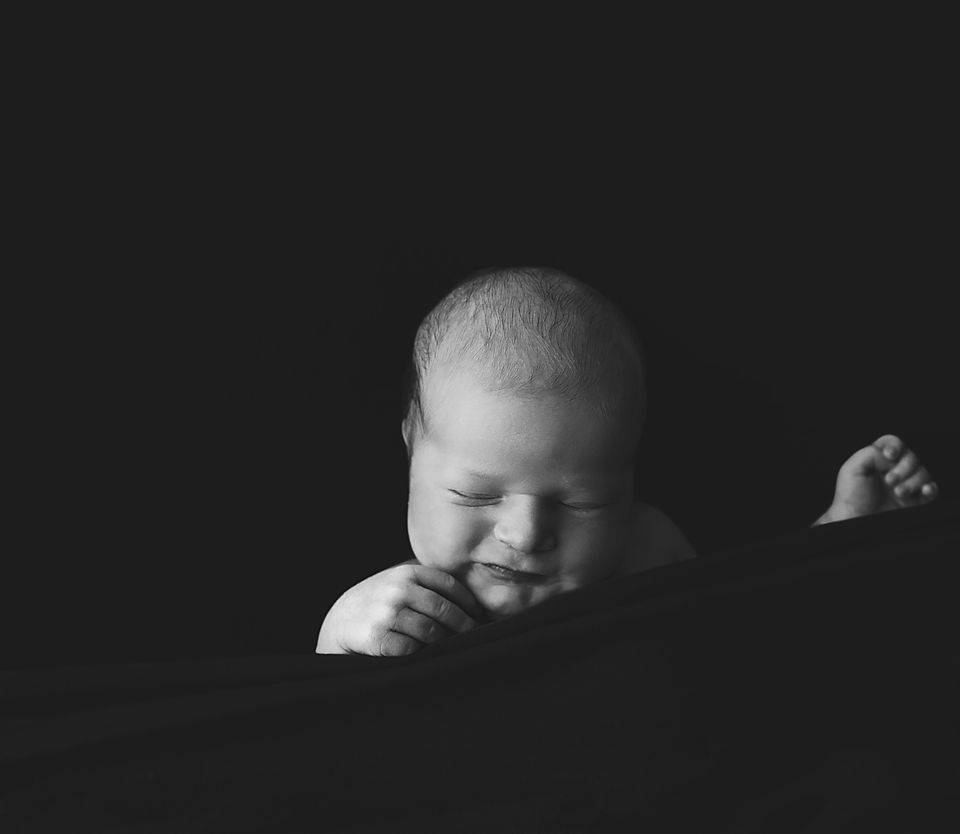 Black and white artistic portraits of a sleeping newborn in dramatic lighting.