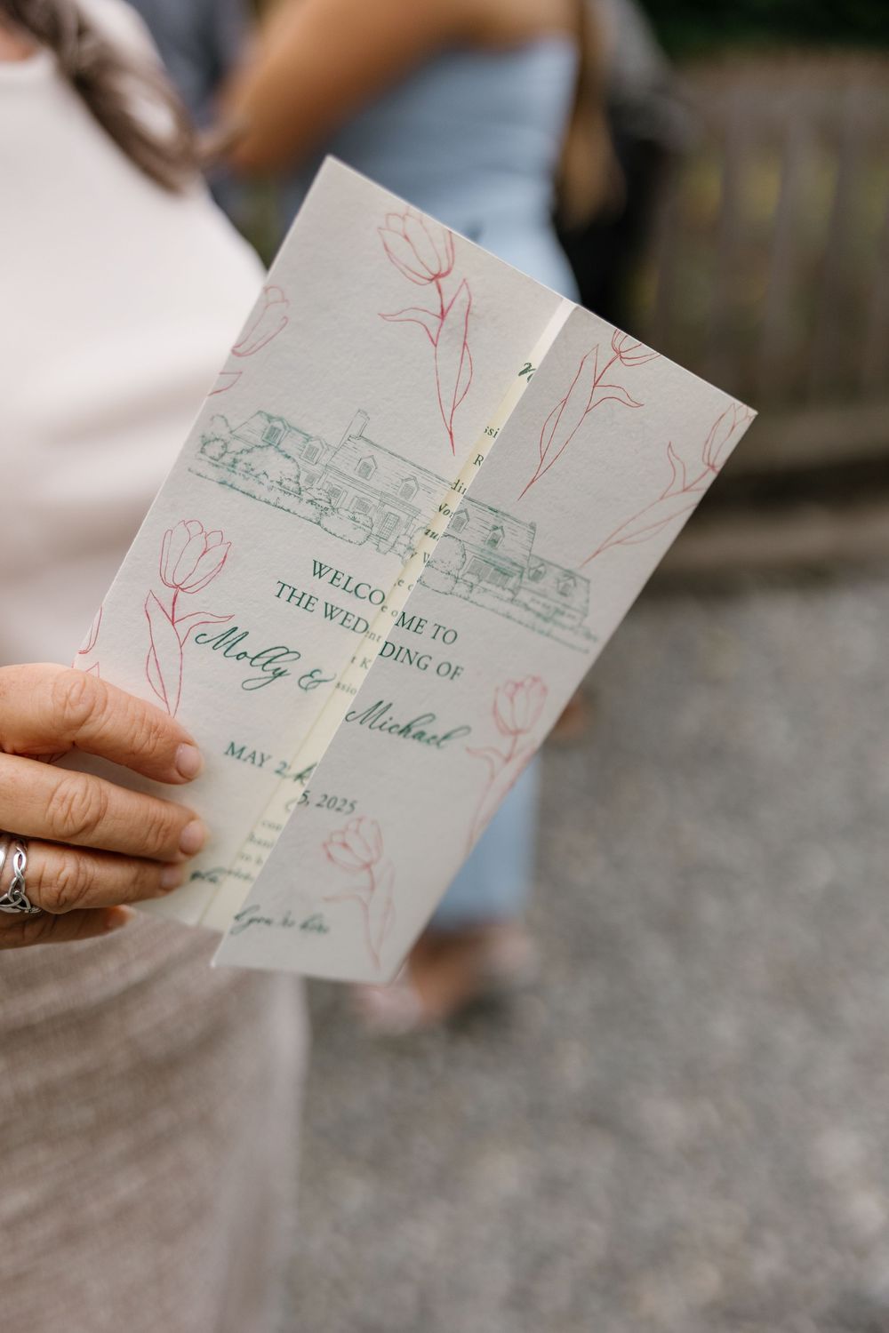 A hand holds an elegant wedding invitation featuring delicate red floral designs and calligraphy text.