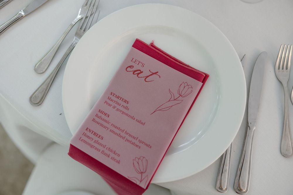 A formal place setting with white plates, silverware, and red menu cards arranged on a white tablecloth.
