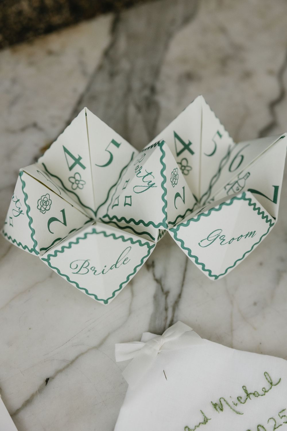 Paper fortune teller with green numbers and 'Bride' text sits on marble surface for wedding entertainment.