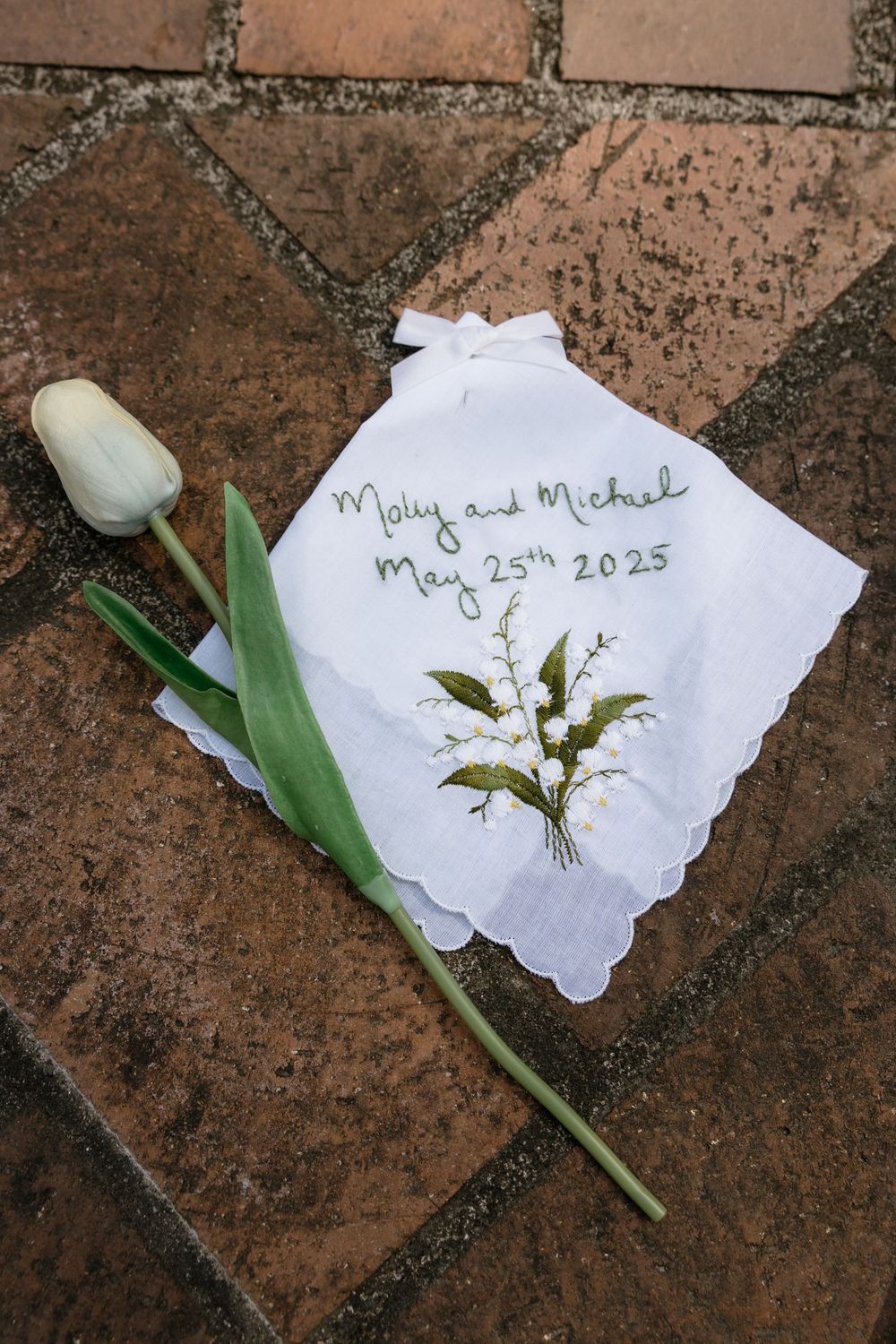 A white handkerchief with pressed flowers and a single tulip stem arranged on terracotta tiles.