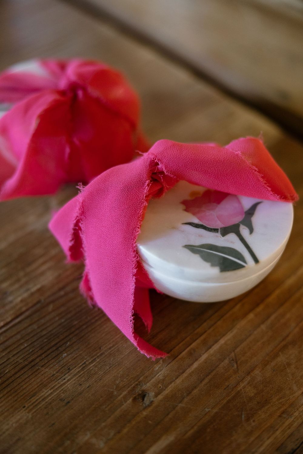 Pink fabric ribbon tied around a white button rests on a rustic wooden surface in macro detail.