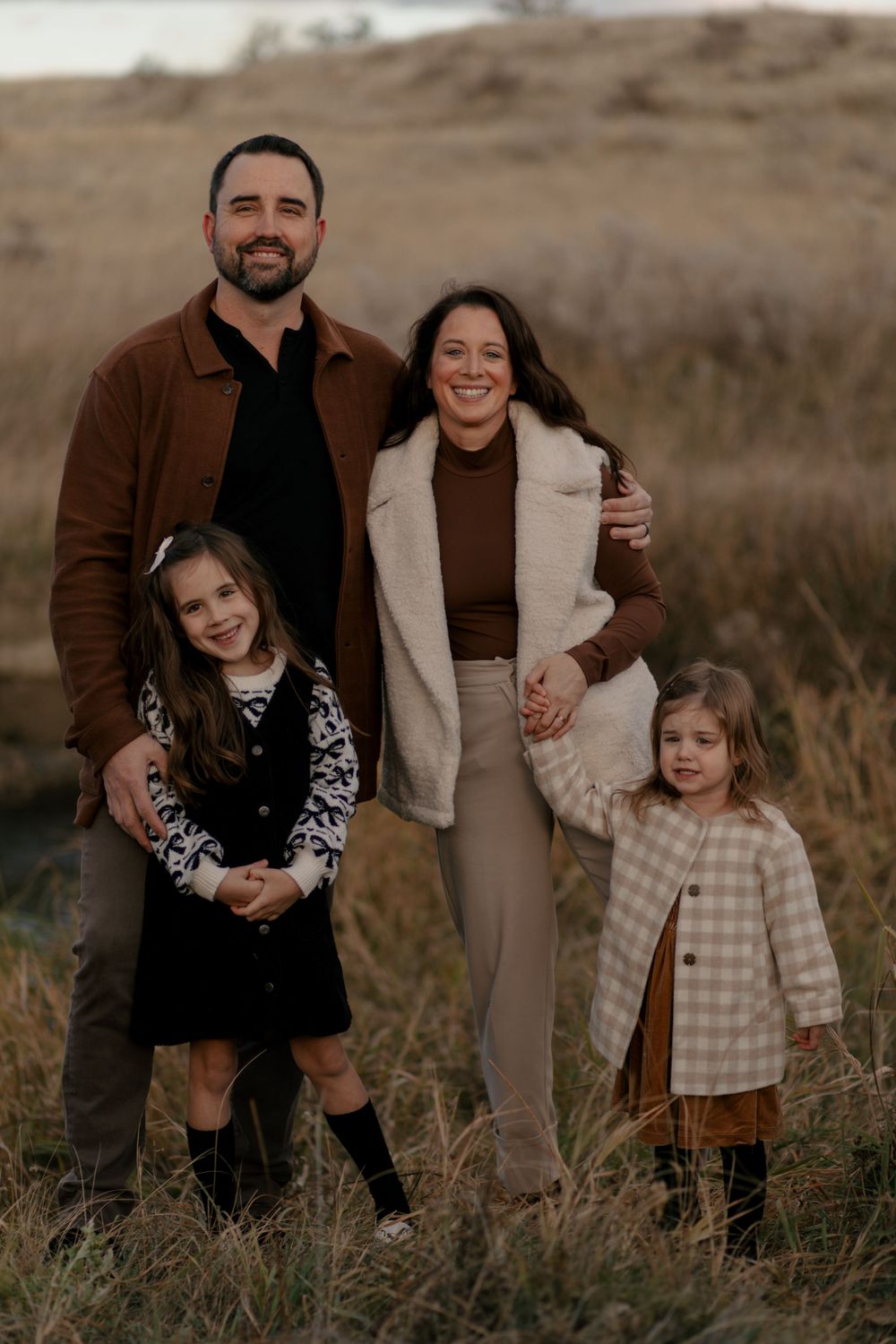 A family of four poses together outdoors in coordinated fall outfits against a natural landscape.