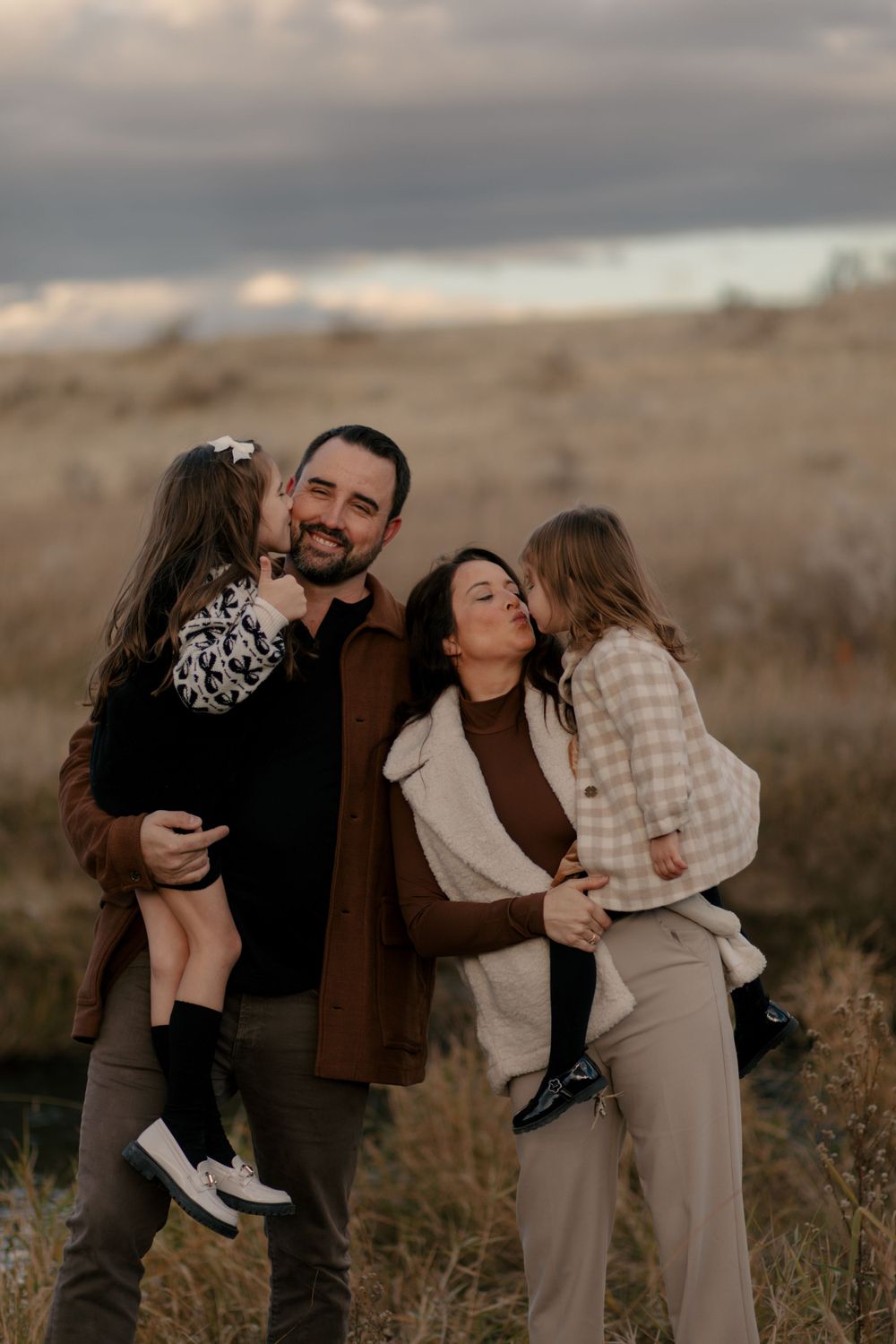 A family of four poses together in warm earth tones against a moody autumn landscape.