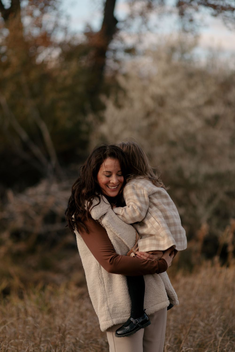 A joyful embrace between adult and child wearing cozy neutral-toned clothing in an autumn setting.