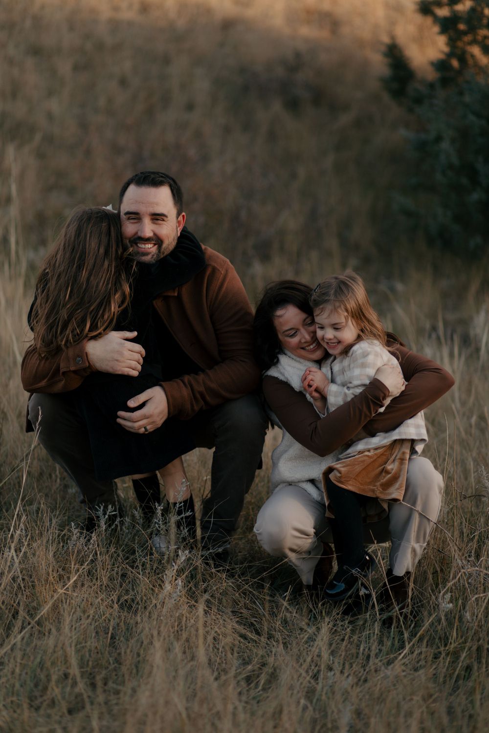 A family shares an intimate moment of laughter while huddled together in a field at sunset.