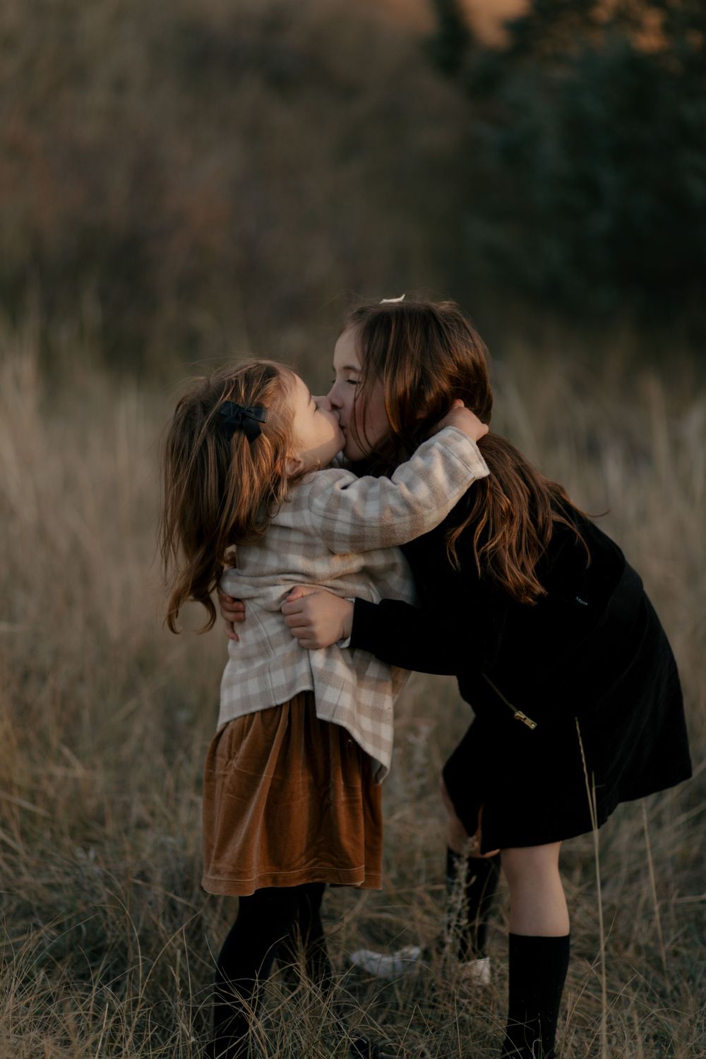 Two children share a sweet moment together in a field during golden hour.