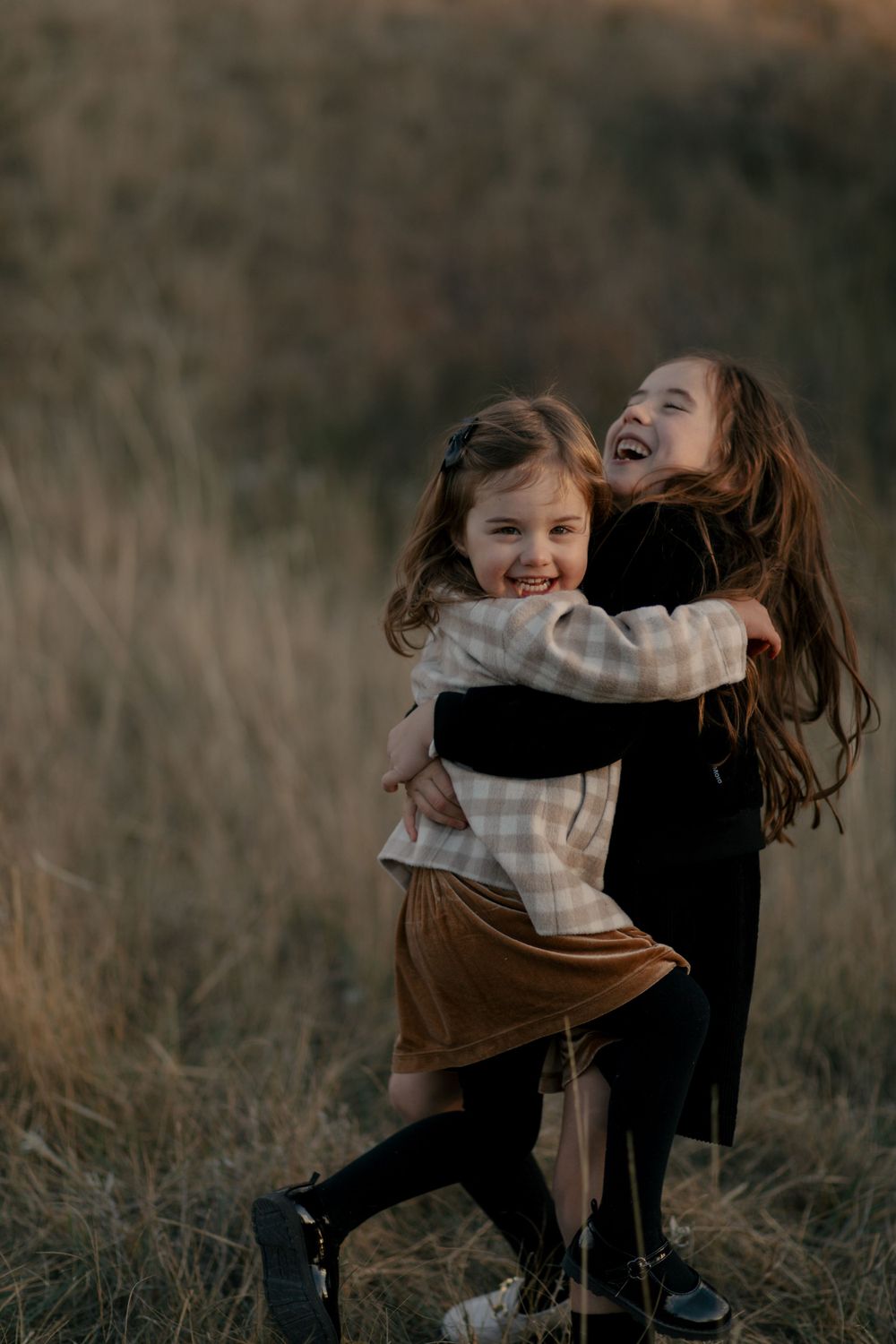 Two children hug and laugh together while playing outdoors in autumn.