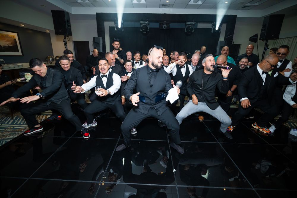 Large group in formal attire poses dramatically on dance floor during wedding celebration.