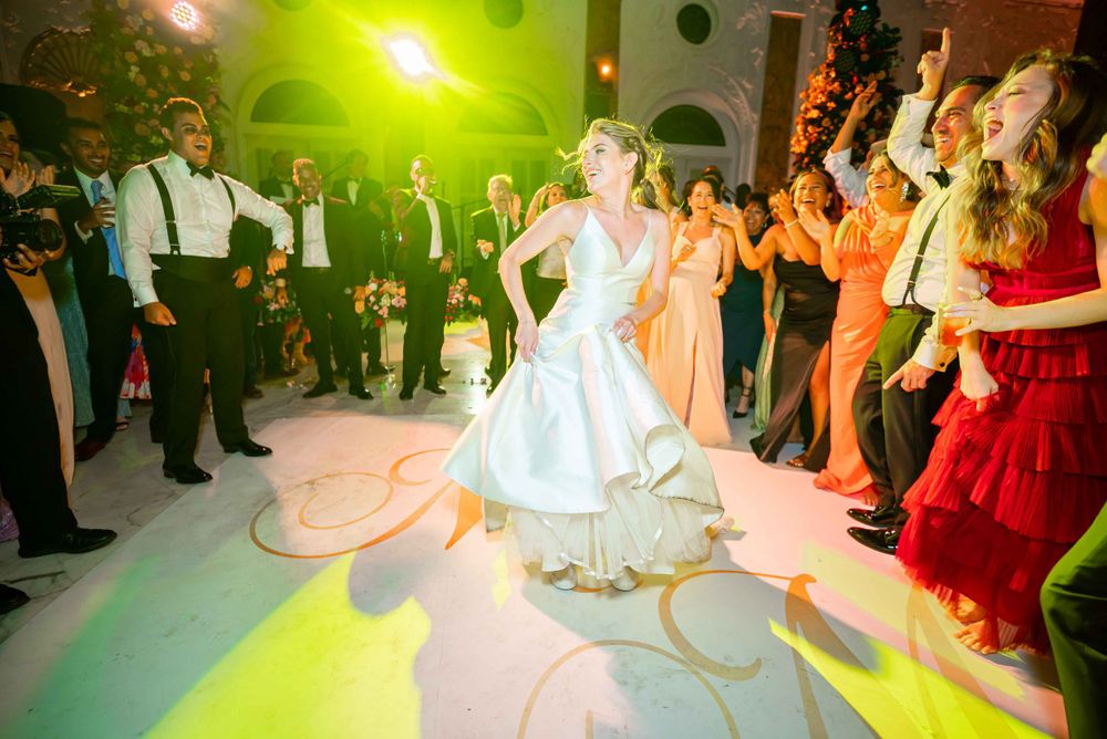 Couple performs romantic first dance on decorated ballroom floor surrounded by wedding guests.