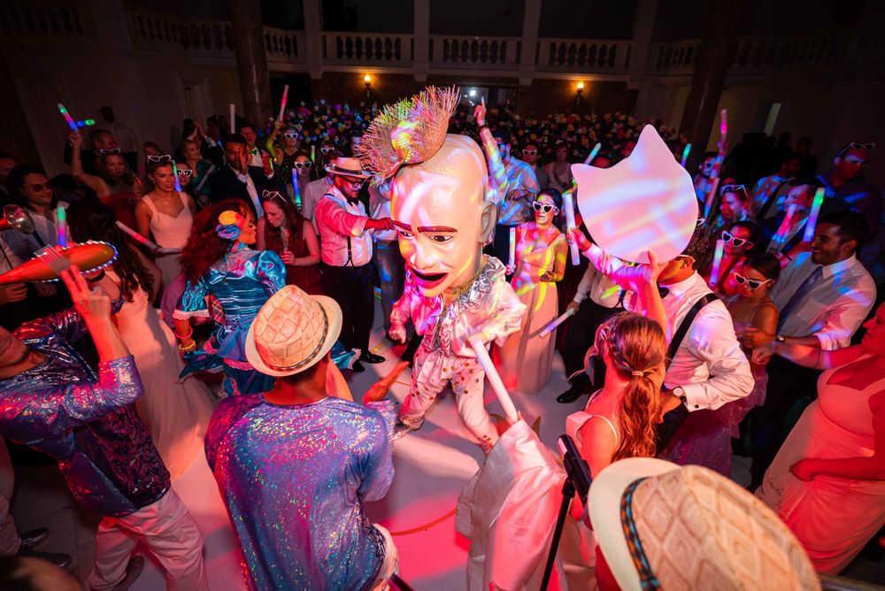 Wedding party dances in vibrant lighting amidst a lively reception celebration.