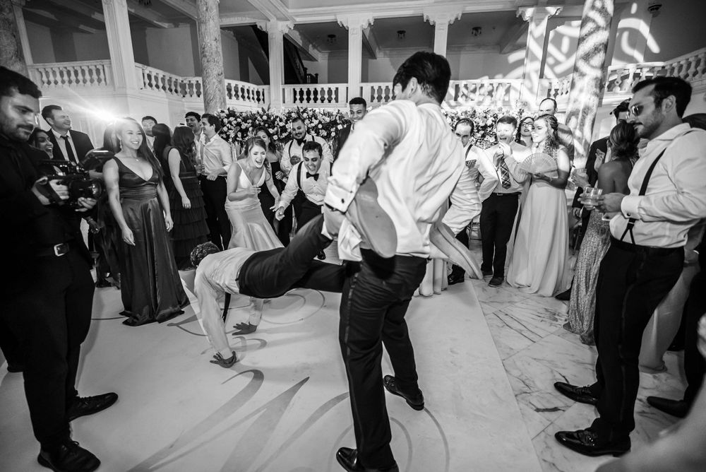 Black and white capture of energetic dance moves during wedding reception entertainment.