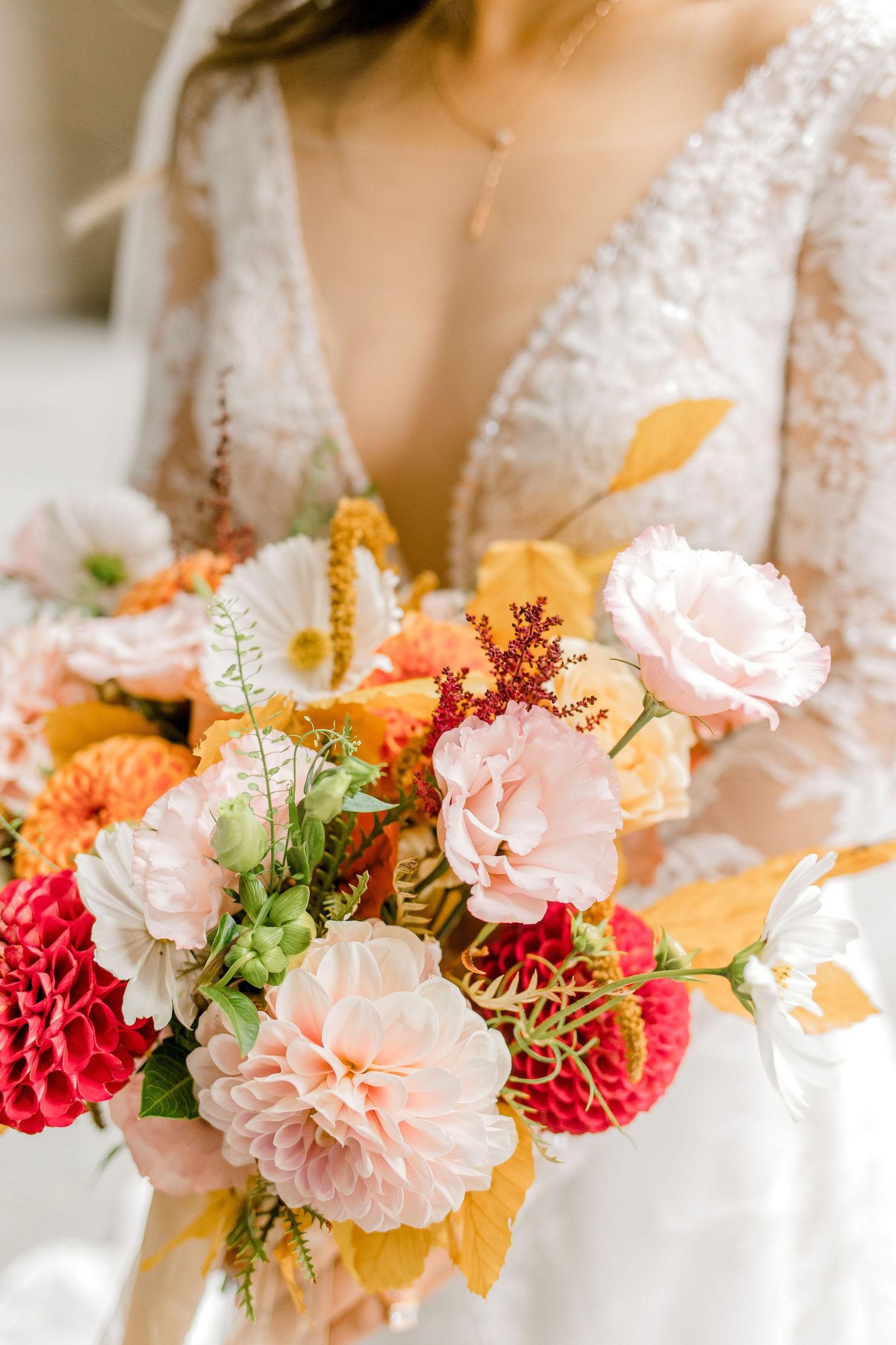 Elegant bridal bouquet featuring pink carnations, red dahlias, and orange blooms with autumn leaves.