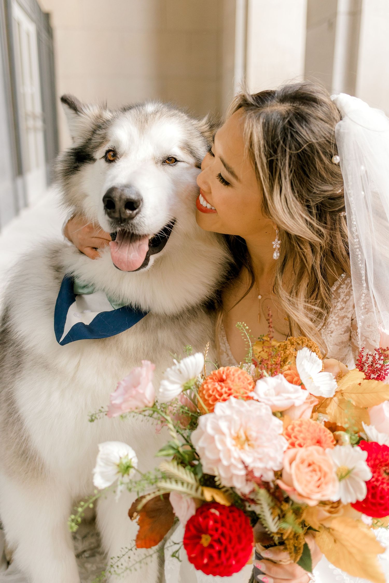 Happy fluffy white dog wearing a blue bowtie poses with wedding bouquet.