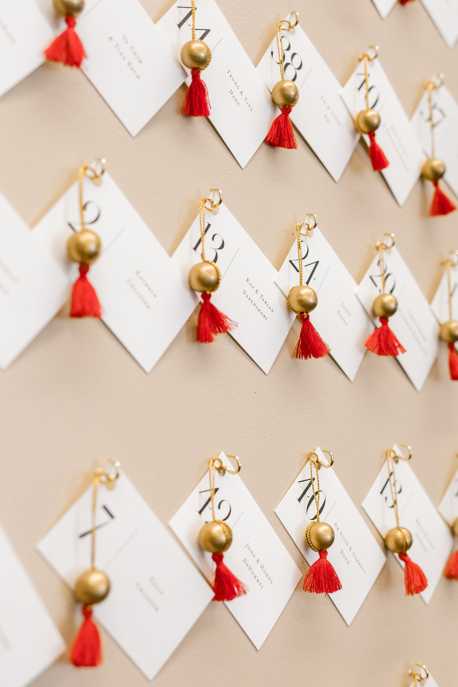 Wedding escort cards decorated with gold bells and red tassels arranged in neat rows.