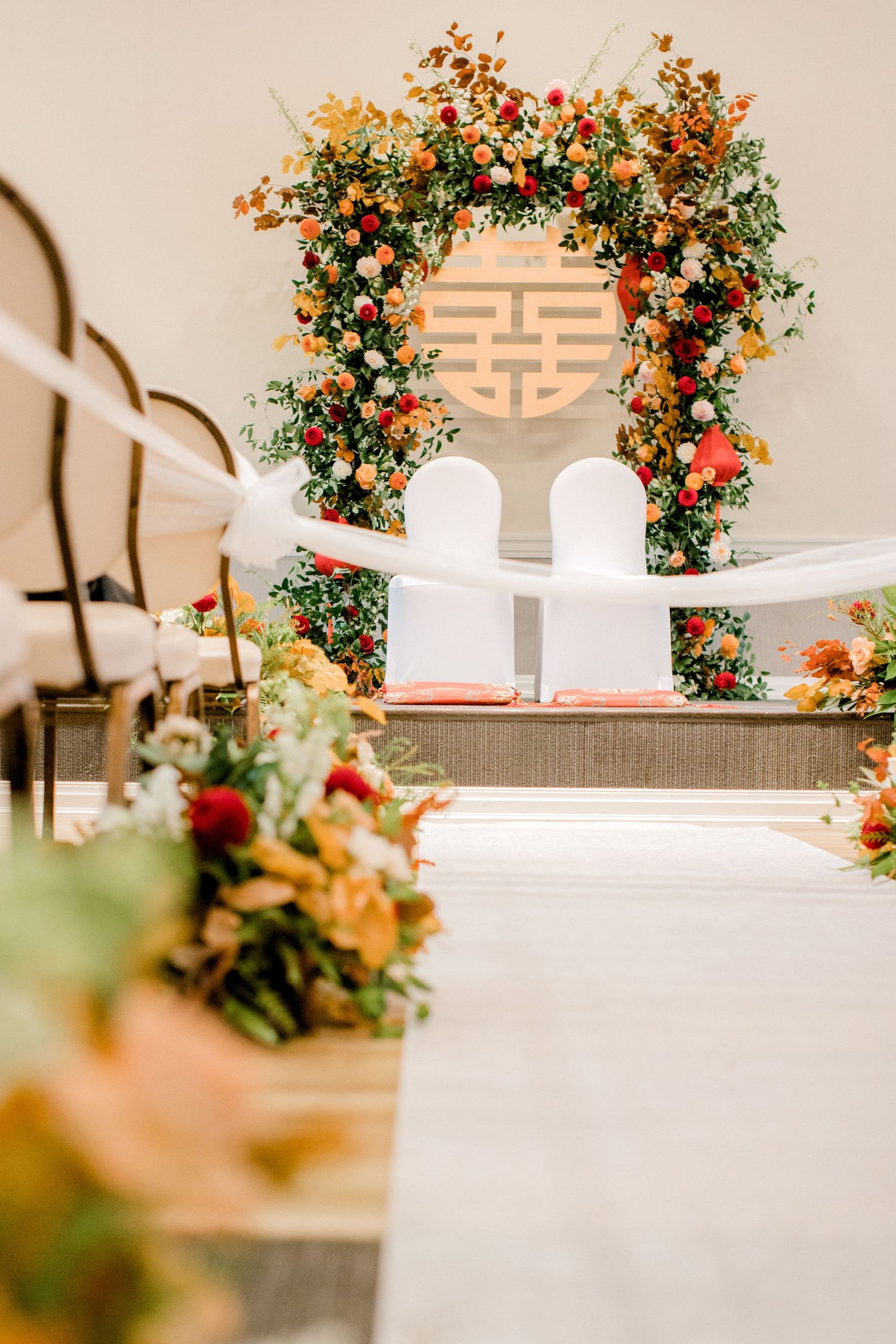 Wedding ceremony arch decorated with orange and red flowers against a double happiness symbol.