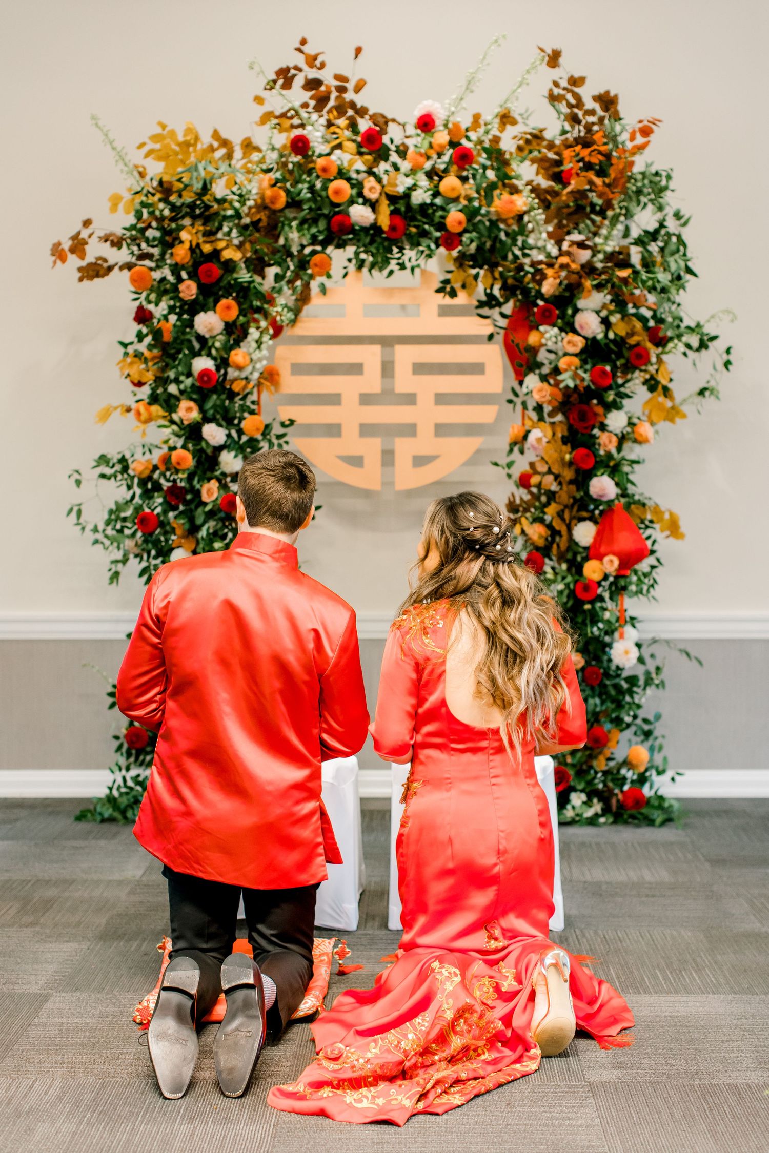 Traditional Chinese double happiness symbol decorated with lush floral arch in red and coral tones.
