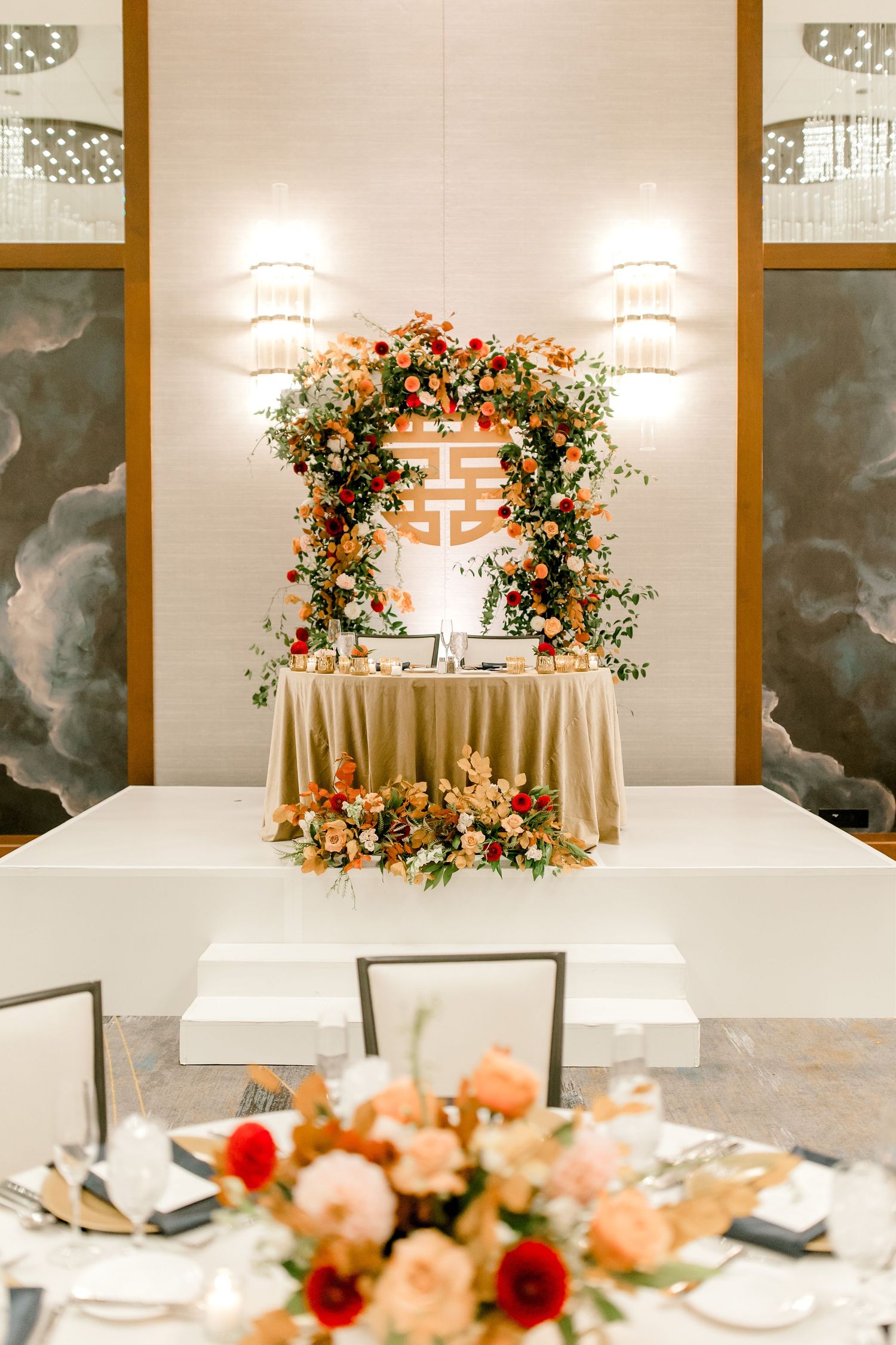 Elegant wedding reception setup with floral arch and double happiness symbol above sweetheart table.