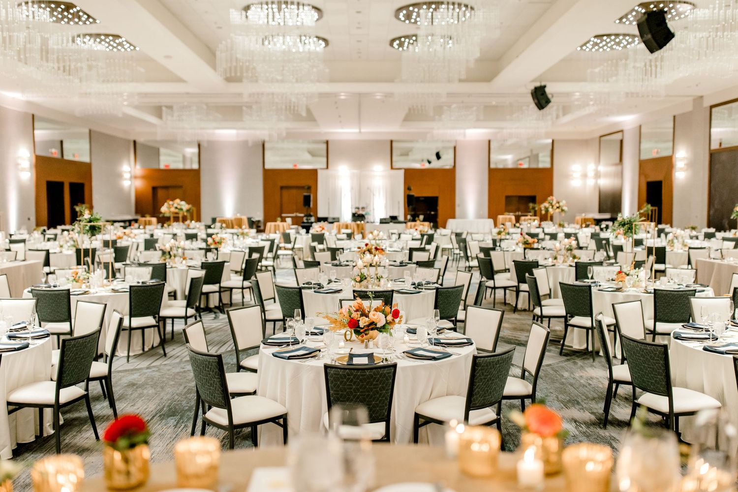 Large elegant ballroom setup with round tables and crystal chandeliers for wedding reception.
