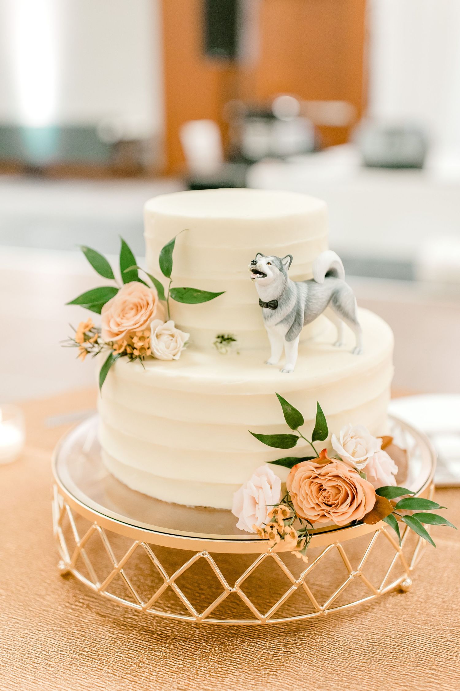 White wedding cake decorated with peach roses and a small husky figurine topper.
