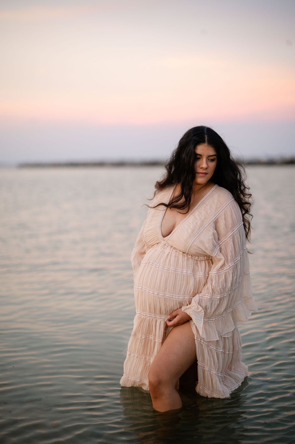 Panama City Beach photographer, family photos PCB, 30A maternity photo with subject standing in calm waters wearing a flowing peach gown.